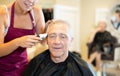 Female hairdresser working hair clipper with older man