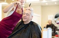 Young female hairdresser working with scissors and comb with mature man