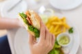 Young female hand holding her half eaten salmon sandwich with the blurred background of french fries Royalty Free Stock Photo