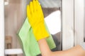 Young female hands cleaning window at home with green rag and protective yellow gloves
