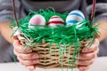 Girl hands with Easter colorful eggs in a wooden basket with green grass