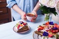 Young female hands holding cup of tea near plate with sour cream cake with fruits decorated with flowers