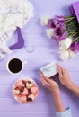 Young female hands holding gift box near bouquet of purple and white tulips, cup of coffee, strawberry in chocolate and hanger wit Royalty Free Stock Photo