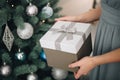 Young female hands holding gift box near the Christmas tree. New Year atmosphere Royalty Free Stock Photo