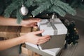 Young female hands holding gift box near the Christmas tree. New Year atmosphere Royalty Free Stock Photo