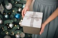 Young female hands holding gift box near the Christmas tree. New Year atmosphere Royalty Free Stock Photo