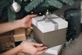 Young female hands holding gift box near the Christmas tree. New Year atmosphere Royalty Free Stock Photo