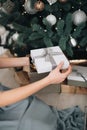 Young female hands holding gift box near the Christmas tree. New Year atmosphere Royalty Free Stock Photo