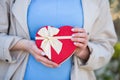 Young female hands holding gift box in shape of red heart with bow Royalty Free Stock Photo