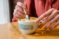 Young female hands with long fingers holding cup of coffee with latteart at table in cafe, woman stirs foam with spoon