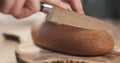 Young female hands slicing rye wheat rustic bread on cutting board