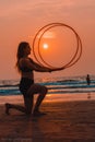 Young female is having fun on a beach during the beautiful sunset, spinning a hula hoops Royalty Free Stock Photo