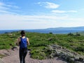 A young female hiker hiking along a trail through a meadow with the beautiful blue atlantic ocean in the background