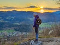 Young female hiker stands on top of hill with her senior dog inside her backpack