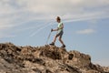 Young female hiker walking with sticks on the rocks