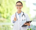 Young female Hispanic doctor wearing a labcoat and smiling while using a digital tablet and showing thumbs up in her Royalty Free Stock Photo