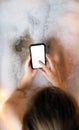 Young female holding blank mobile phone, smart phone in bathtub with soapy foam close-up top view background