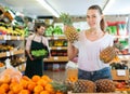 Young female holding fresh pineapples in fruit store