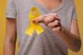 Young female holding yellow gold ribbon awareness symbol for endometriosis, suicide prevention, sarcoma bone cancer