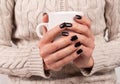 Young Female holds tea cup in hands with black nail and sweater