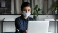 Young female indian professional in facemask working on computer.