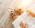 Young female inspecting a city map resting on the bed with untied trekking boots on wooden floor