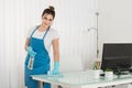 Young Female Janitor Using Spray To Wipe Desk Royalty Free Stock Photo