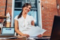 Young female journalist preparing a new article holding papers using laptop sitting at desk in creative office Royalty Free Stock Photo