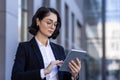 A young female lawyer is standing outside the courthouse in a business suit and glasses and is seriously using a tablet Royalty Free Stock Photo