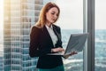 Young female lawyer working in her luxurious office holding a laptop standing against panoramic window with a view on Royalty Free Stock Photo