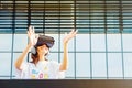 Young female with long hair and white t-shirt wearing virtual reality glasses and big headphones while raising hands in front of