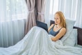 Young female lying in bed in morning, holding tablet computer, watching videos, reading news, looking relaxed and calm