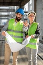 Young female and male engineers or business partners at construction site, discussing plans and examining works. Architecture and Royalty Free Stock Photo