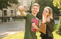 Young female and male friends in the park posing for selfie on smartphone camera, millenial students taking photo on mobile phone Royalty Free Stock Photo