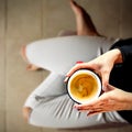 Young female manicured hands holding cup of coffee with fresh foam on floor background.