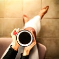 Young female manicured hands holding cup of coffee with fresh foam on floor background.