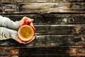 Young female manicured hands holding cup of coffee with fresh foam on old dark rustic wooden table background.