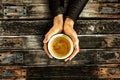 Young female manicured hands holding cup of coffee with fresh foam on old dark rustic wooden table background.