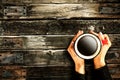 Young female manicured hands holding cup of coffee with fresh foam on old dark rustic wooden table background.