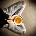 Young female manicured hands holding cup of hot coffee with fresh foam on floor background.