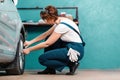Young female mechanic in blue coveralls squatting and repair tire with ratchet wrench. The concept of women& x27;s Royalty Free Stock Photo