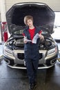 Young female mechanic reading paper with open bonnet of car in garage