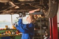 Young female mechanic works under the car