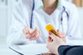 Young female medicine doctor sitting in front of working table holding jar of pills and explains to the patient how to Royalty Free Stock Photo