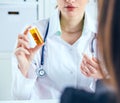 Young female medicine doctor sitting in front of working table holding jar of pills and explains to the patient how to Royalty Free Stock Photo