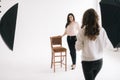 Young female model posing with chair in photo studio for female photographer. Royalty Free Stock Photo