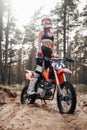 Young female motocross racer in safety helmet riding on her motorcycle in off road adventure