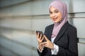 Young Female Muslim Entrepreneur smiling, holding her smartphone.