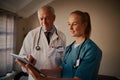 Young female nurse in conversation with senior male doctor discussing medical reports on digital tablet in hospital Royalty Free Stock Photo