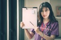 Young female nurse holding pencil and showing her clipboard